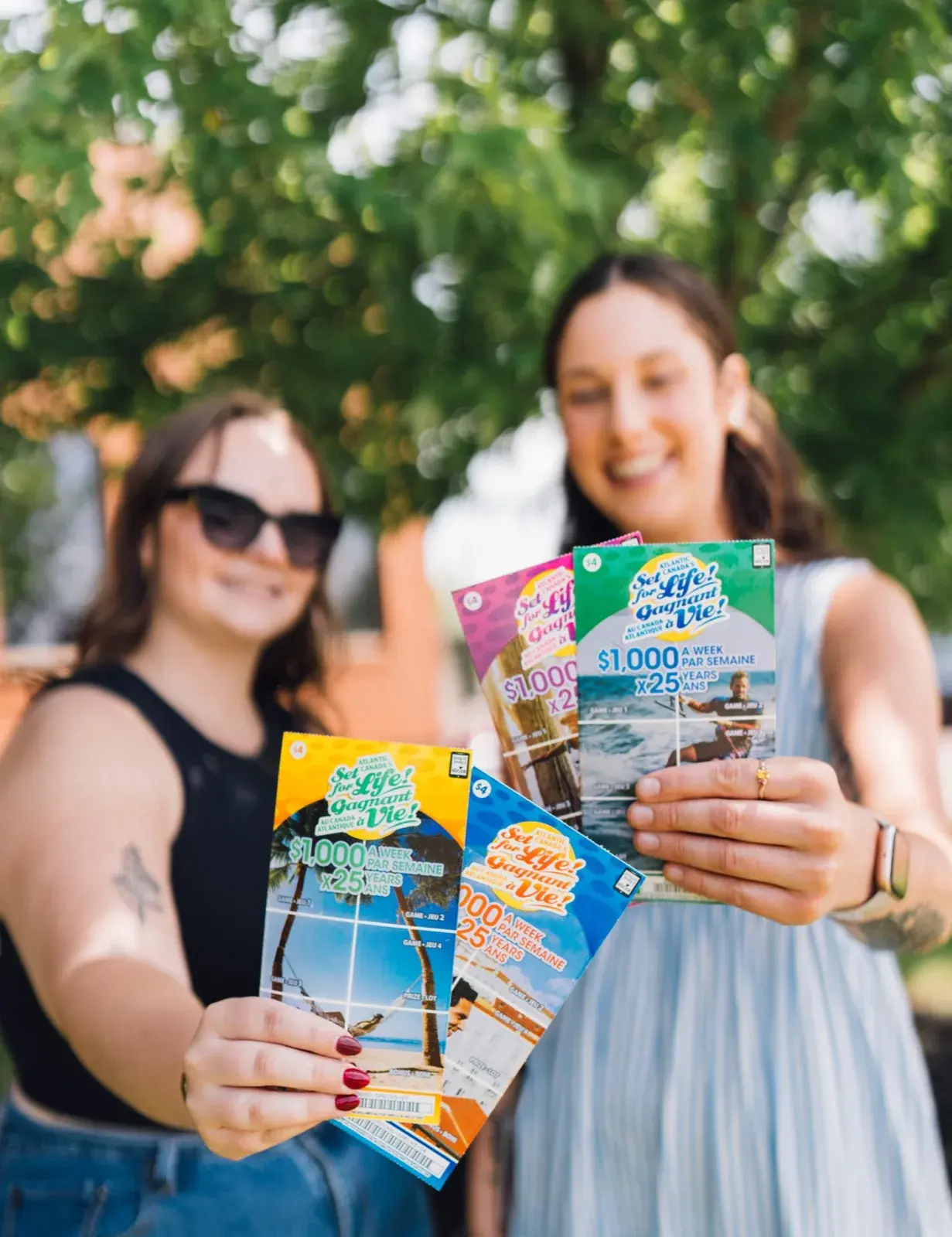 Deux femmes souriantes tenant des billets à gratter Gagnant à vie