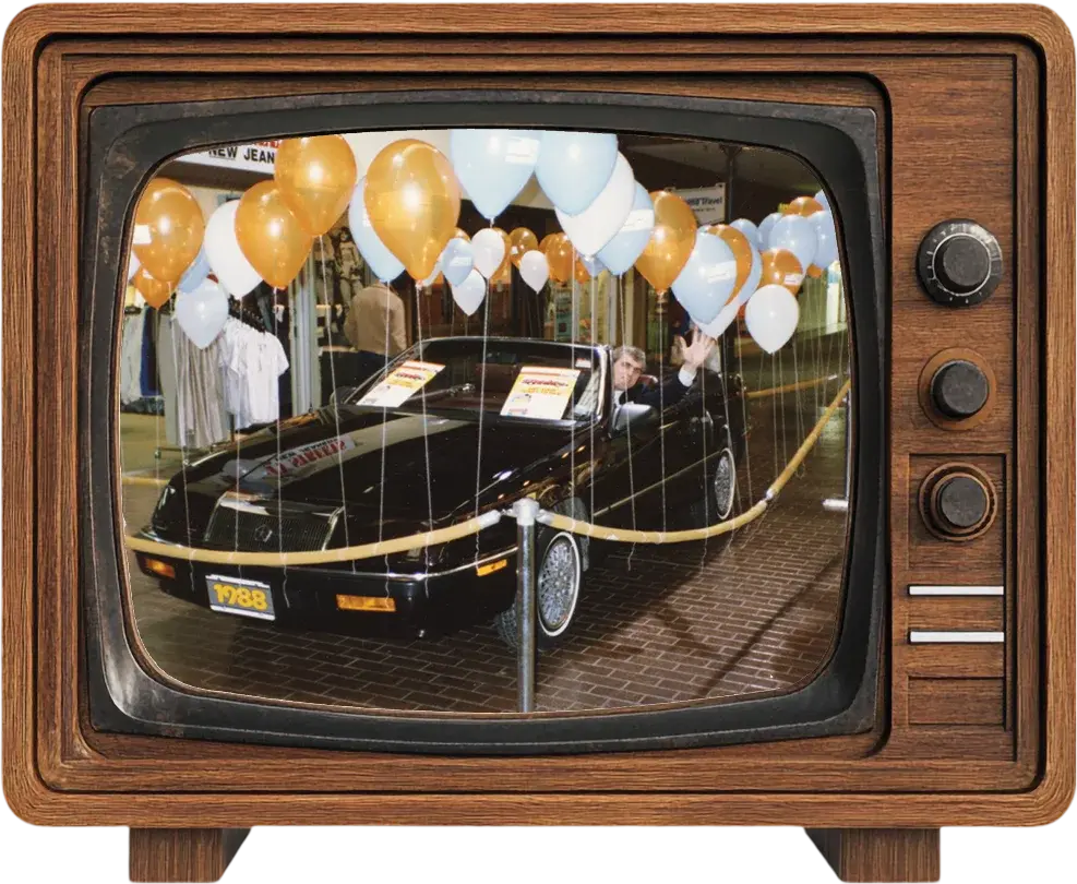 Un téléviseur d’époque montrant une voiture à gagner de 1988 entourée de ballons lors d’une promotion dans un centre commercial